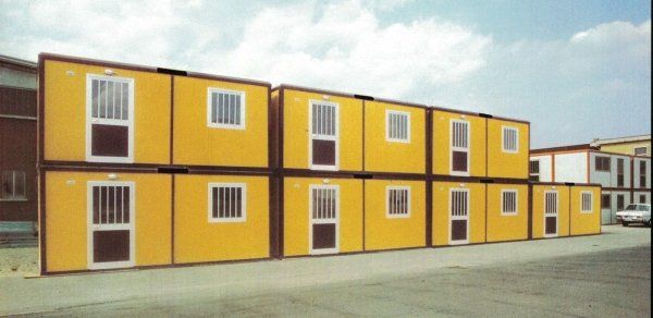 Una fila di due piani di container modulari gialli adibiti a ufficio, dotati di porte e finestre, disposti su un lotto pavimentato.