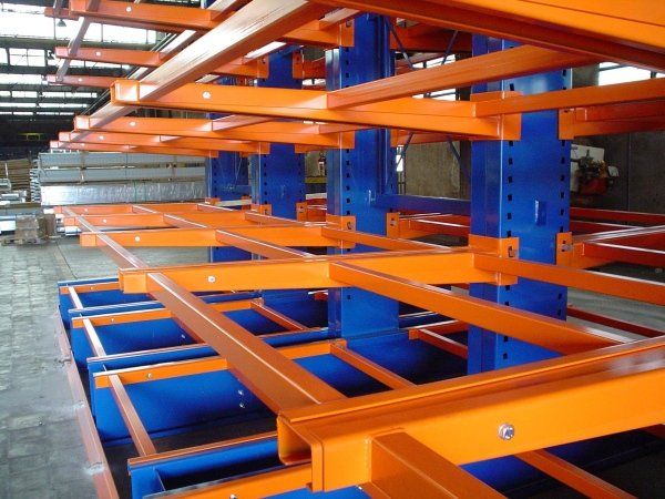Scaffalature a sbalzo in metallo arancione con supporti verticali blu in un ambiente di magazzino industriale.