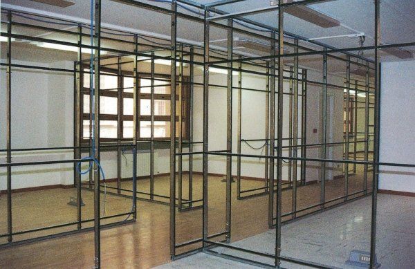 Uno spazio interno che mostra le strutture metalliche delle pareti divisorie installate in un ambiente open space con pavimento di colore chiaro.