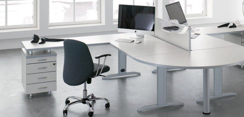 Una moderna postazione di lavoro in ufficio con scrivania angolare bianca, sedia da ufficio grigio scuro e monitor per computer.