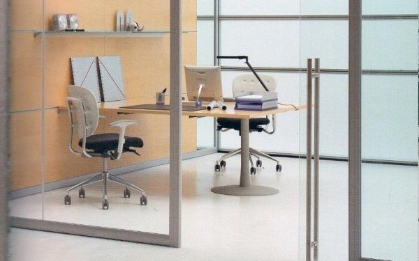 Interno di un ufficio moderno visto attraverso una porta a vetri, con scrivania in legno, due sedie con rotelle e mensola a muro.