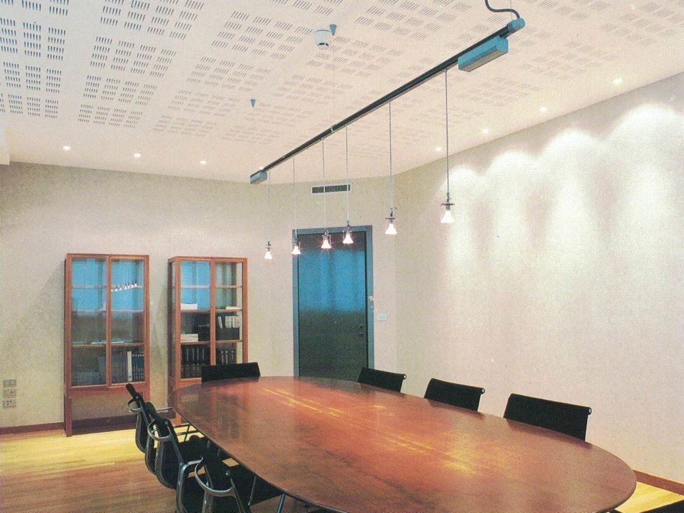 Una sala conferenze con un tavolo ovale in legno, sedie nere e lampade a sospensione appese a un binario sul soffitto.