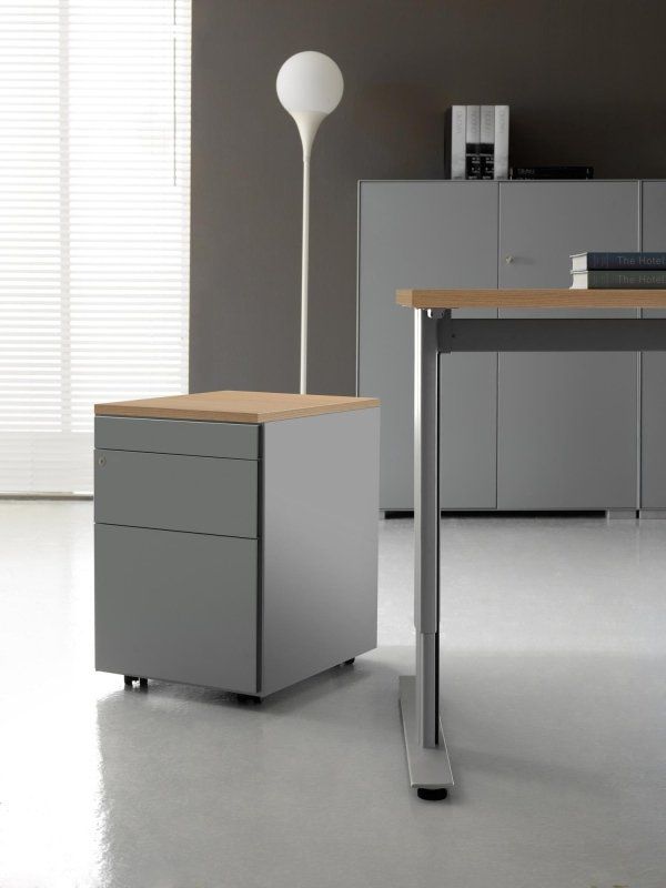 In un ufficio moderno, un mobile contenitore grigio con piano in legno chiaro è posizionato accanto a una scrivania.