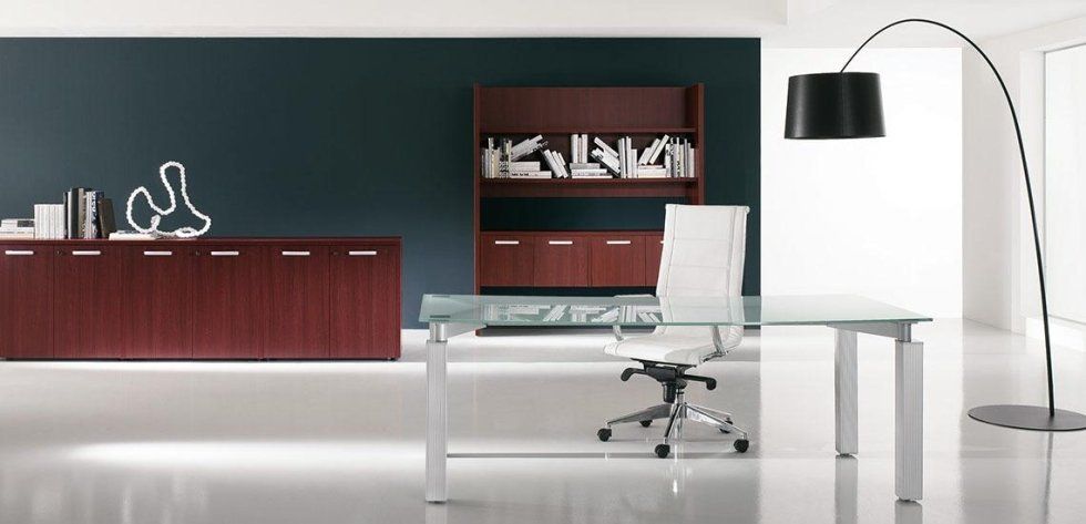 Un moderno ufficio domestico con scrivania con piano in vetro, sedia in pelle bianca, mobili in mogano coordinati e una lampada da terra ad arco alta.