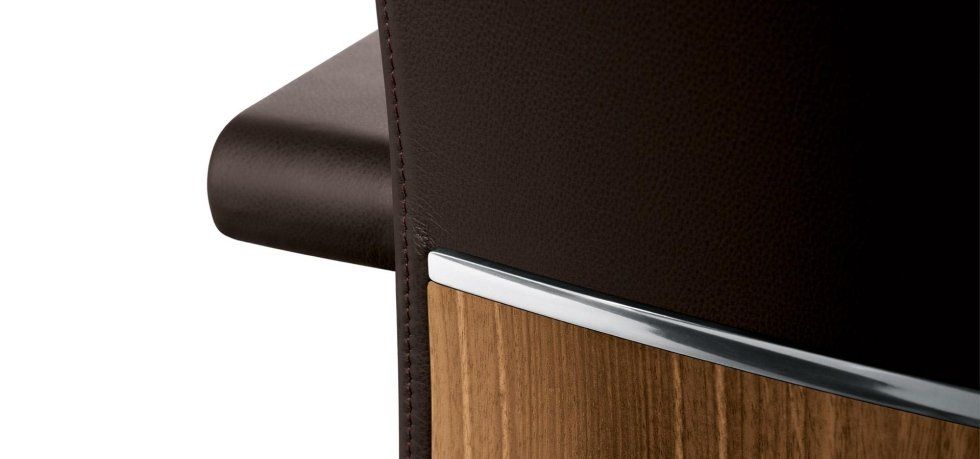 Un primo piano di un rivestimento in pelle scura che incontra un pannello in legno con una finitura argentata.