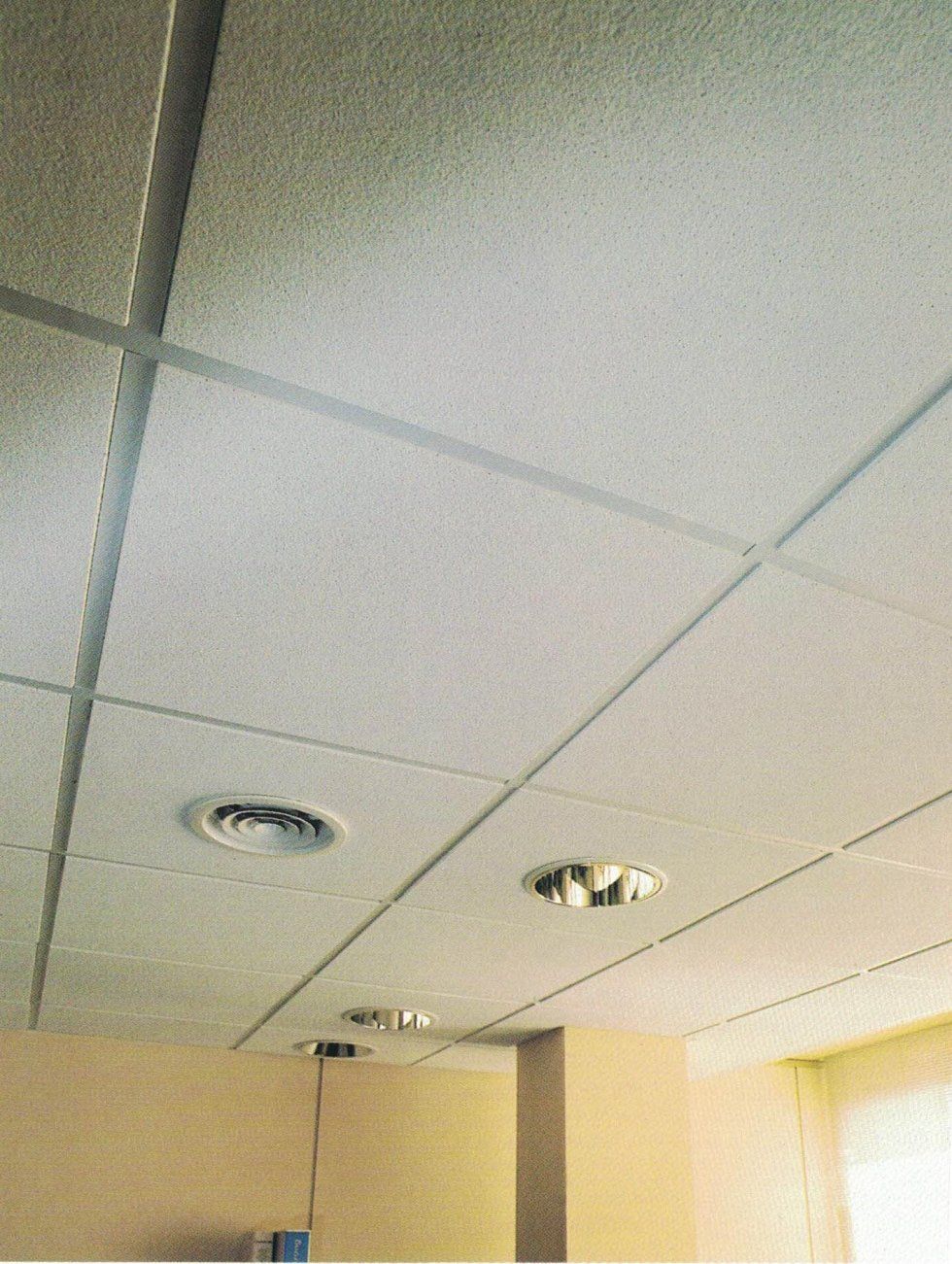 Un controsoffitto bianco con faretti a incasso e una bocchetta di ventilazione circolare in una stanza con parete ad angolo.
