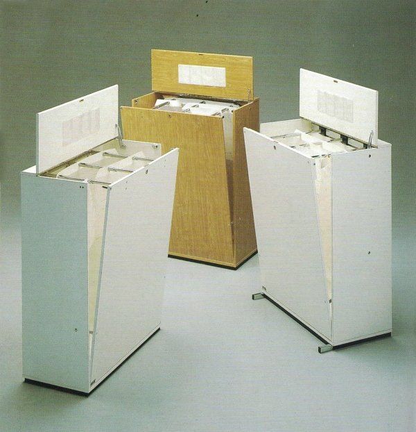 Tre schedari verticali autoportanti, due bianchi e uno in legno chiaro, con coperchi aperti e cartelle sospese.