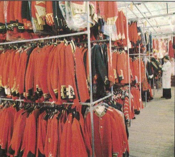 In un magazzino per abiti, file di uniformi militari di colore rosso acceso sono appese a delle grucce, con una persona in piedi nelle vicinanze.