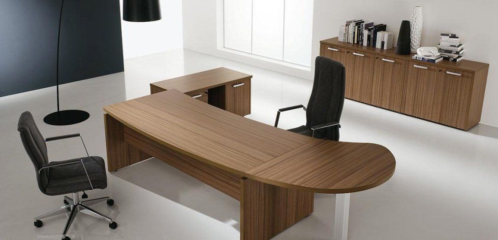 Un ufficio direzionale con una scrivania in legno curvato, due sedie da ufficio nere e una lunga credenza in legno, in una stanza luminosa.