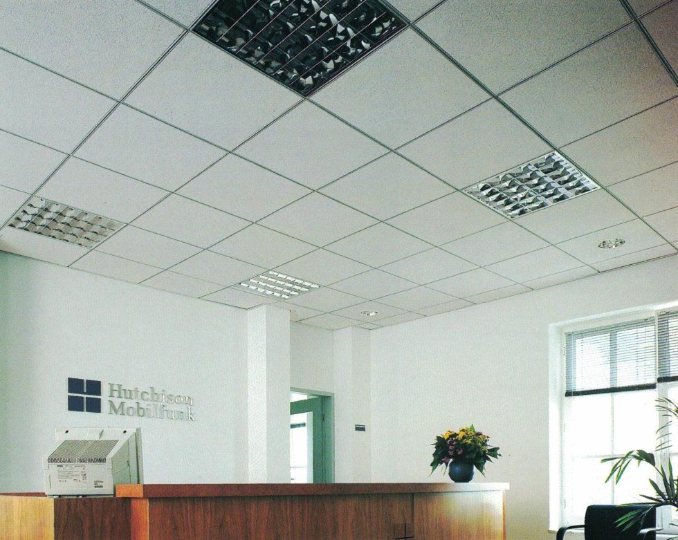 Una reception per ufficio ben illuminata con scrivania rivestita in legno, pareti bianche e controsoffitto rivestito in piastrelle bianche con faretti integrati.