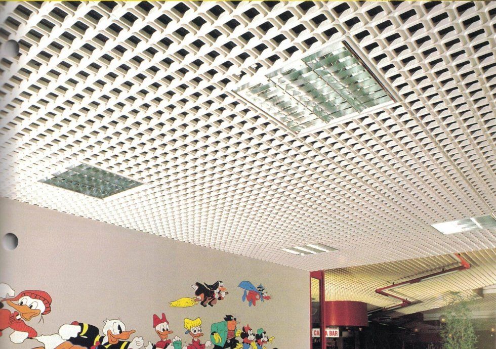 Un controsoffitto a griglia con pannelli luminosi incassati sopra una parete decorata con adesivi colorati raffiguranti personaggi dei cartoni animati.