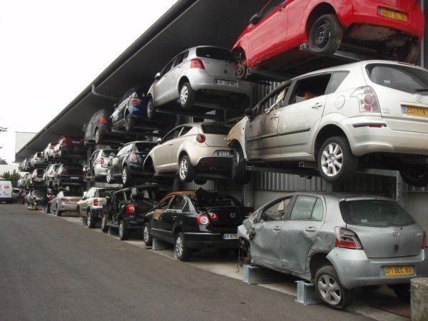 Auto impilate in un parcheggio multipiano, con file di veicoli disposte su diverse mensole metalliche.