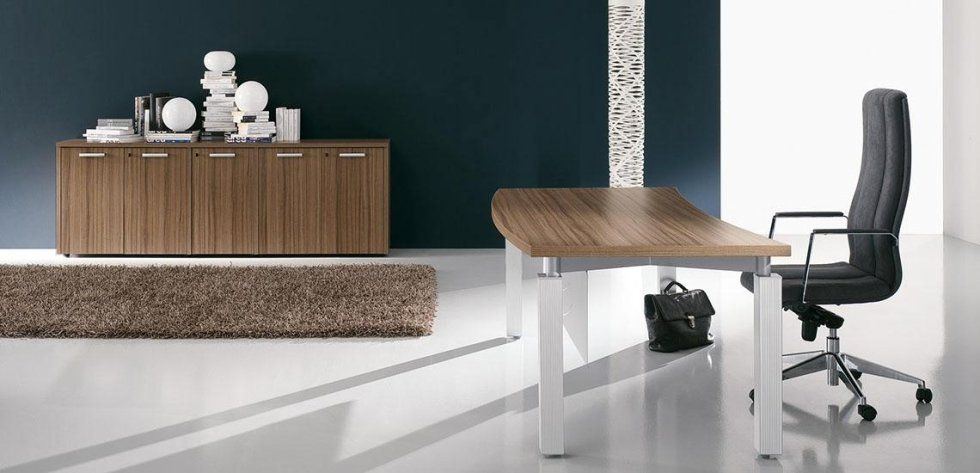 Un moderno spazio ufficio è arredato con una scrivania in legno con gambe bianche, una sedia ergonomica nera e una credenza in legno abbinata.