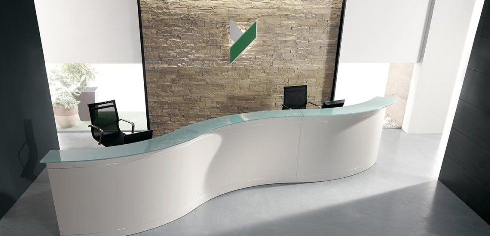 Un bancone reception bianco e curvo è collocato in una hall ben illuminata, addossato a una parete in pietra con il logo aziendale.