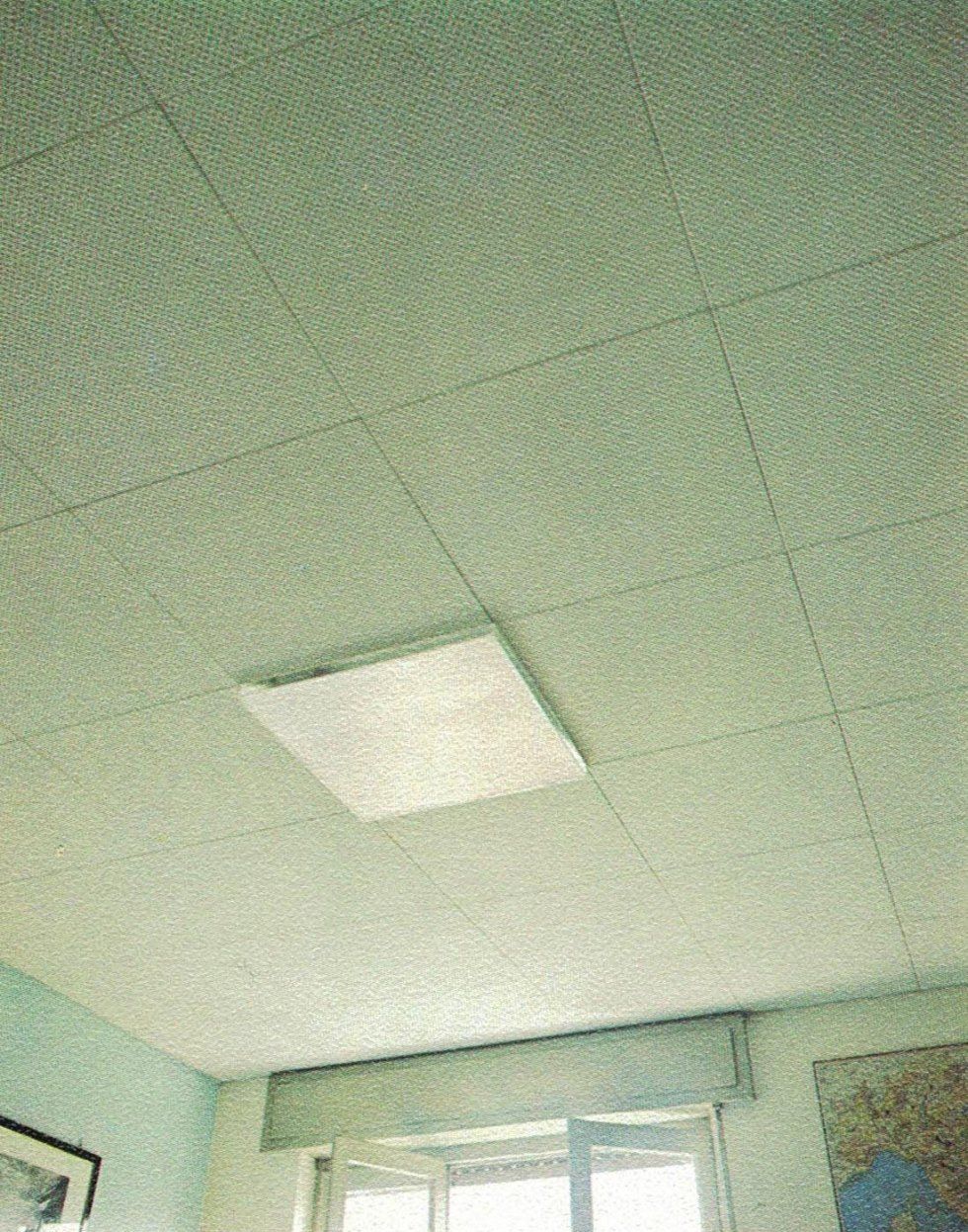 Un apparecchio di illuminazione quadrato centrato in un controsoffitto a pannelli acustici a griglia di colore chiaro.
