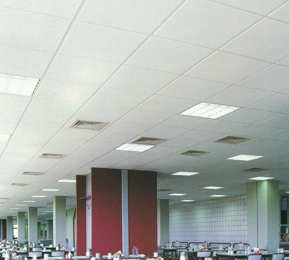 Vista dal basso di un controsoffitto in un ampio ufficio, caratterizzato da file di piastrelle quadrate bianche, faretti a incasso e bocchette di ventilazione.