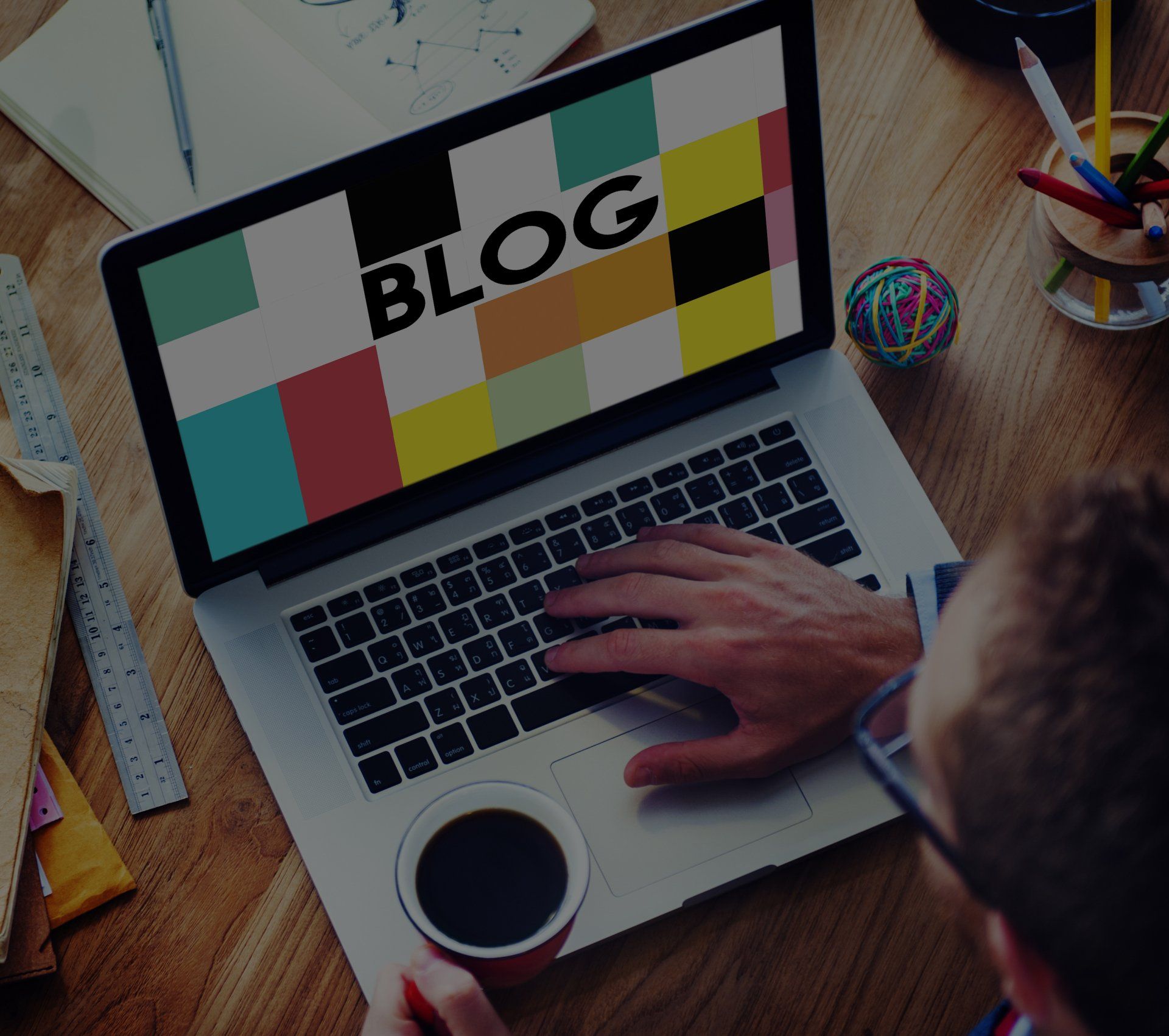Person typing on laptop with “BLOG” on screen, coffee cup, workspace setting.