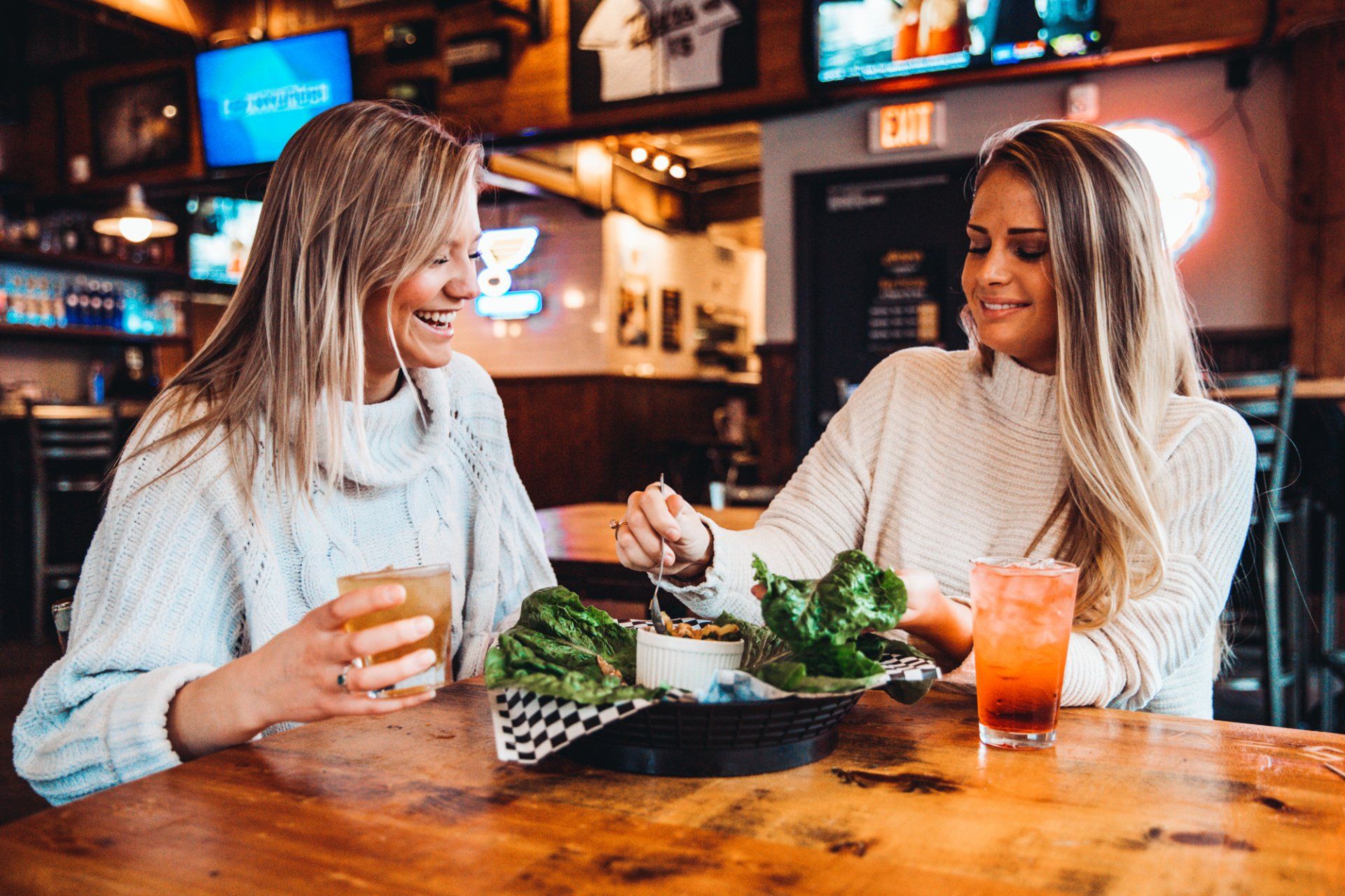 Two women are sitting at a table in a restaurant eating and drinking.