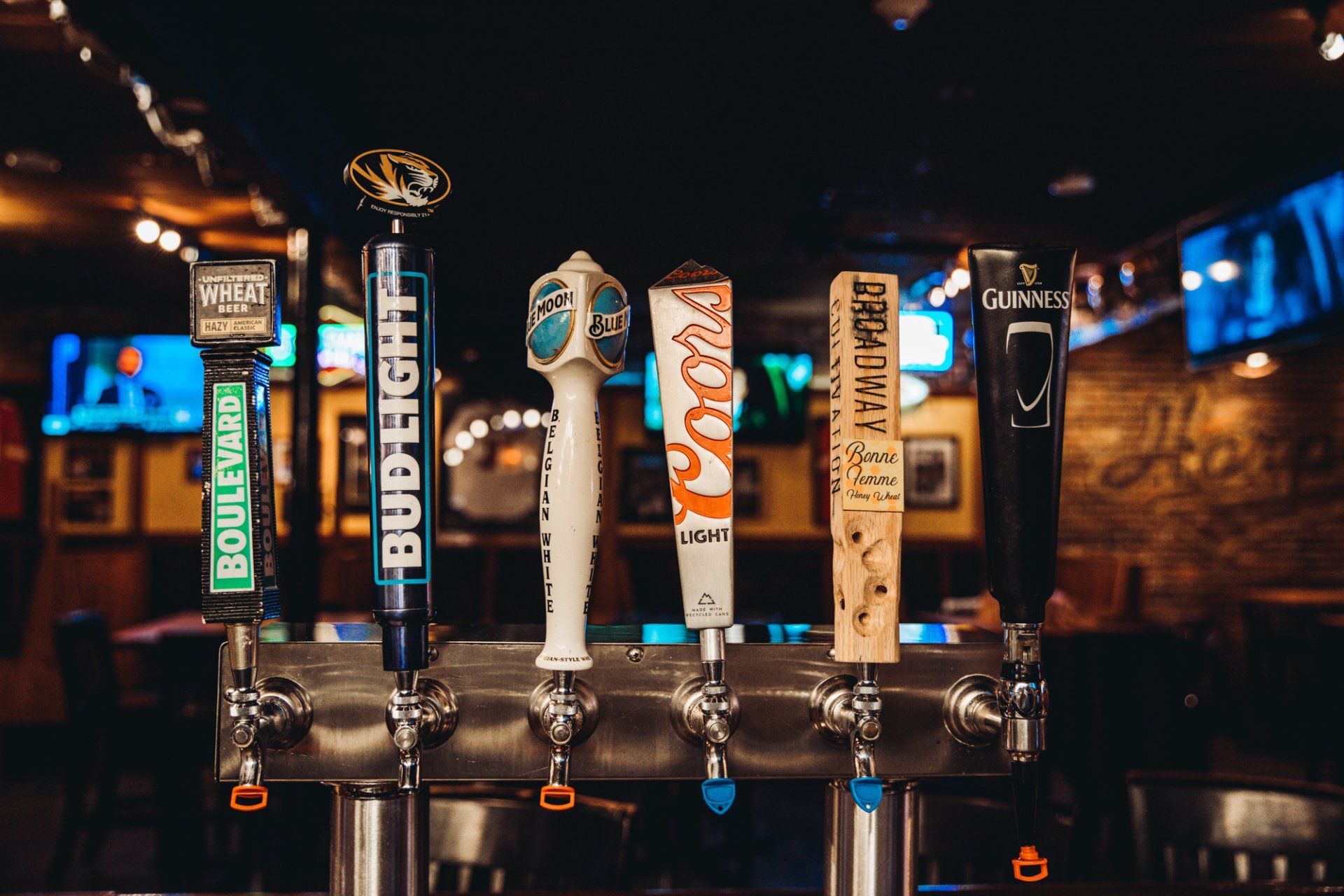 A bunch of beer taps are lined up on a bar.