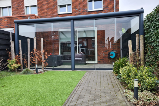 Een bakstenen huis met een glazen overdekt terras in de achtertuin.