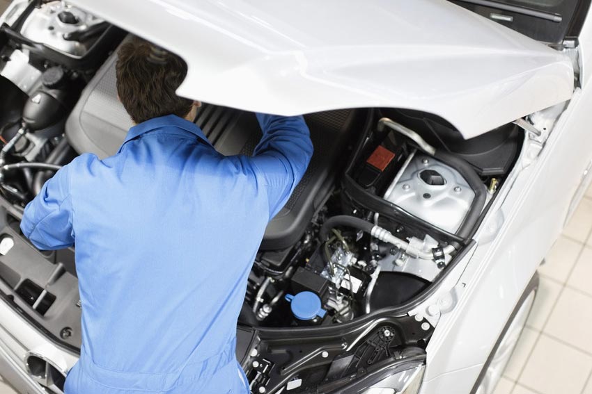 A mechanic under a car bonnet conducting a repair.