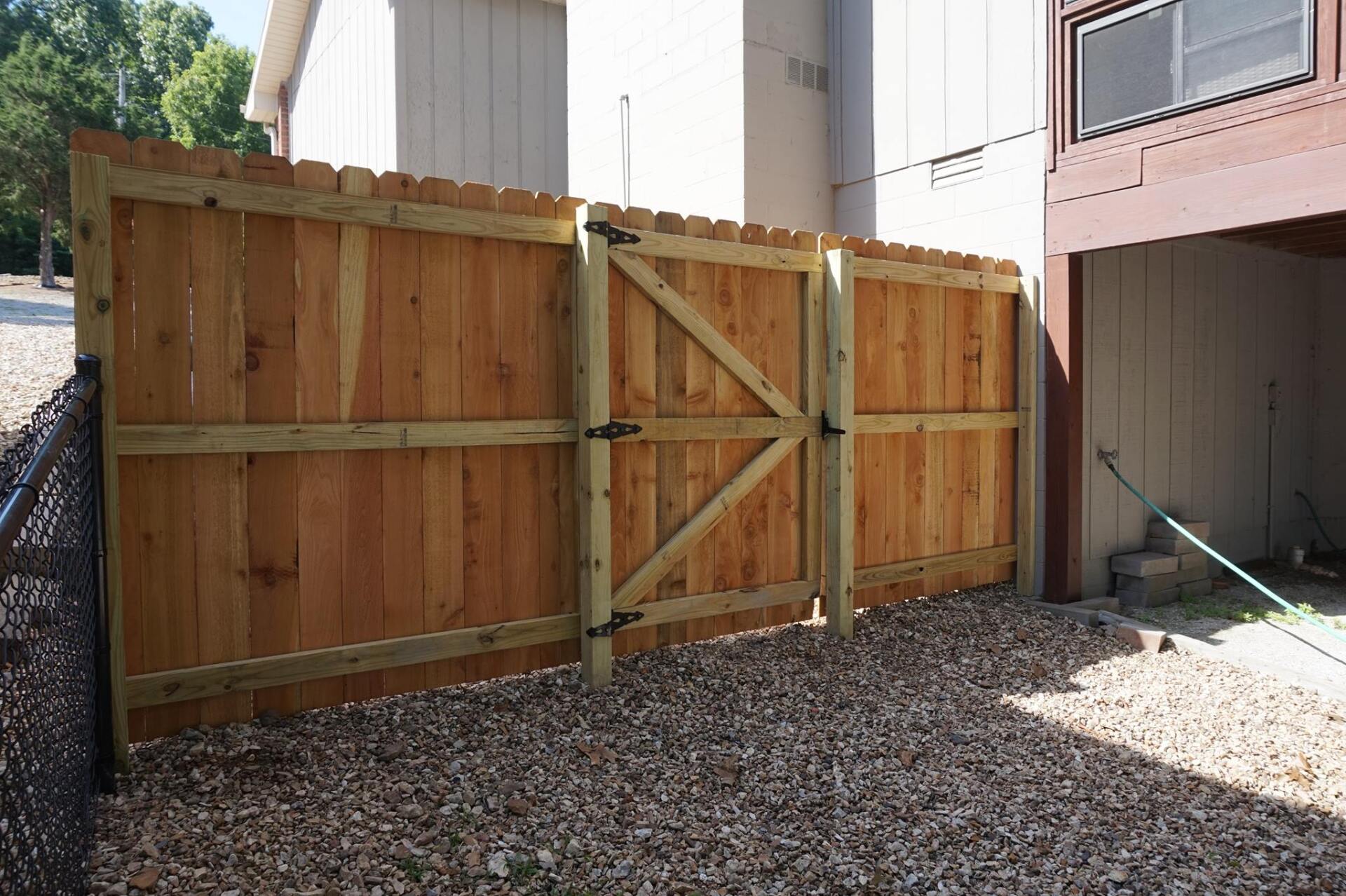 Wooden privacy fence and gate beside a house, with gravel ground and a small walkway on the right.
