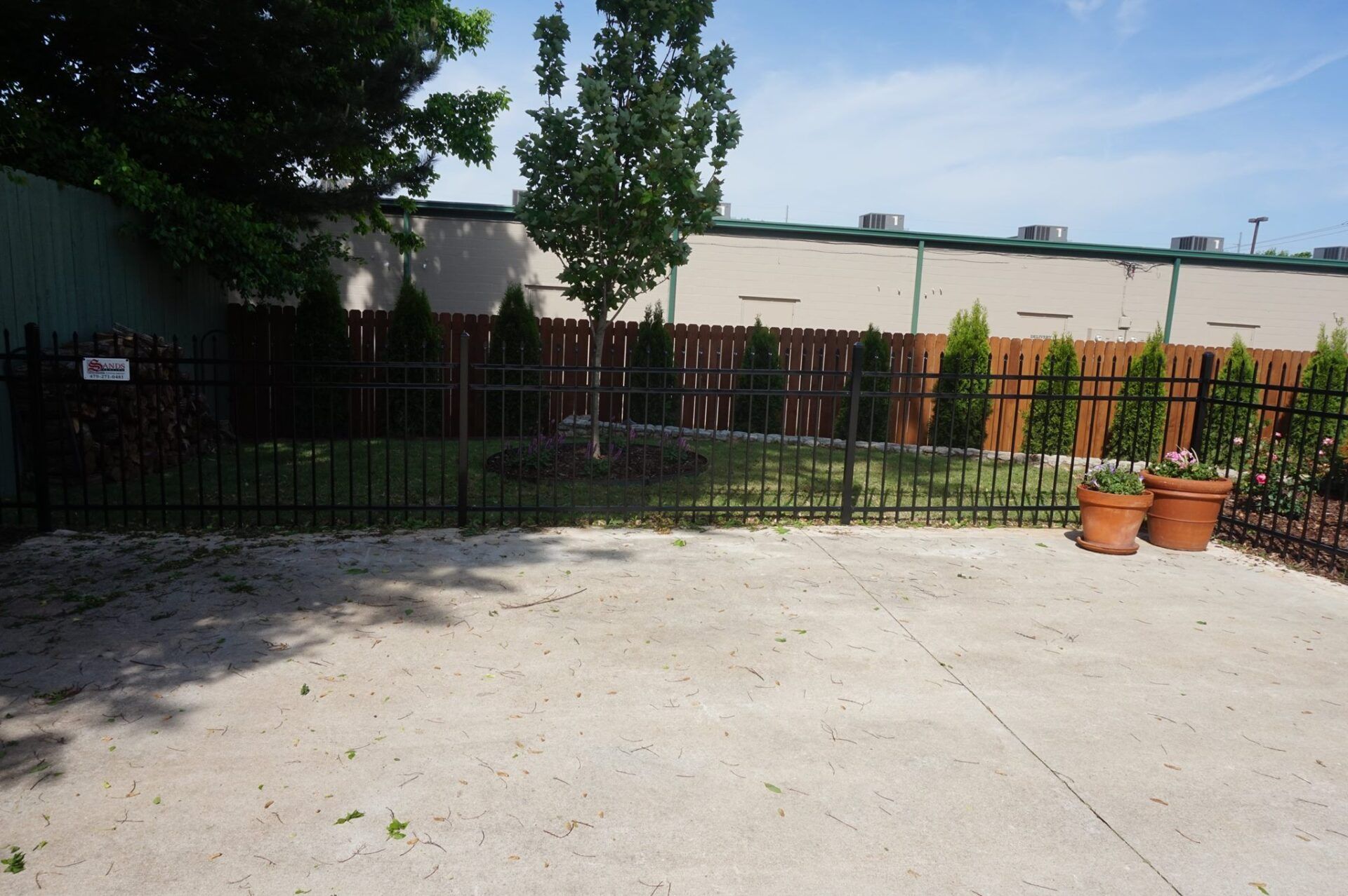 Empty concrete courtyard with a wooden fence, trees, and potted plants in the corner