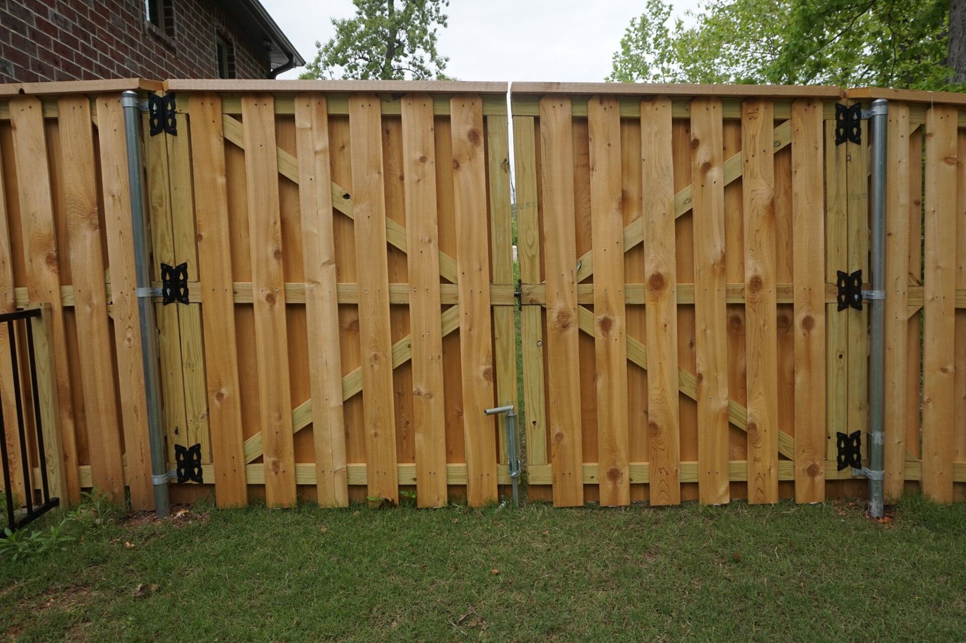 Wooden double gate with metal hinges and latch in a grassy yard, framed by a fence