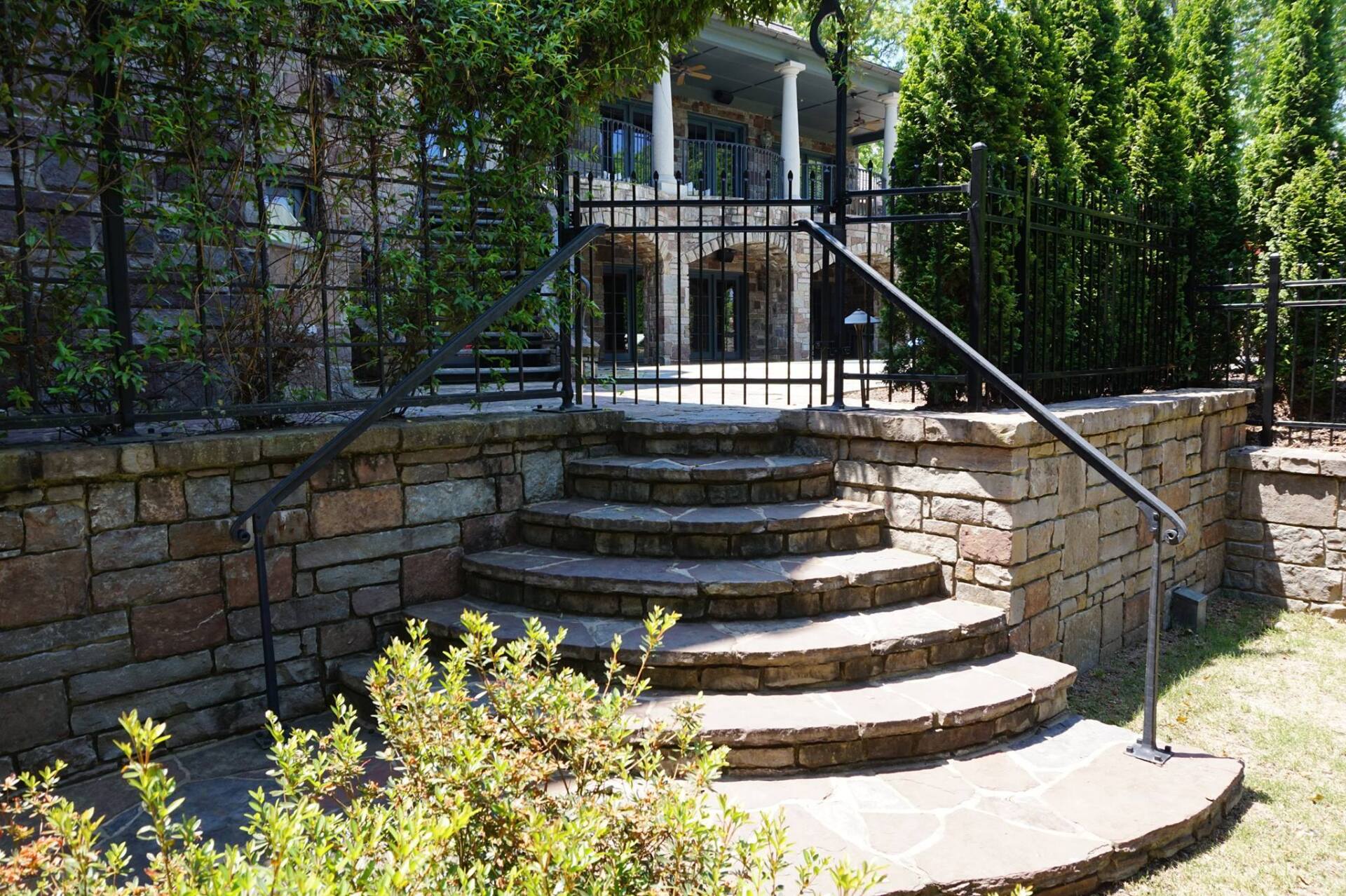 Stone steps leading to a raised patio and black metal gate in a landscaped garden
