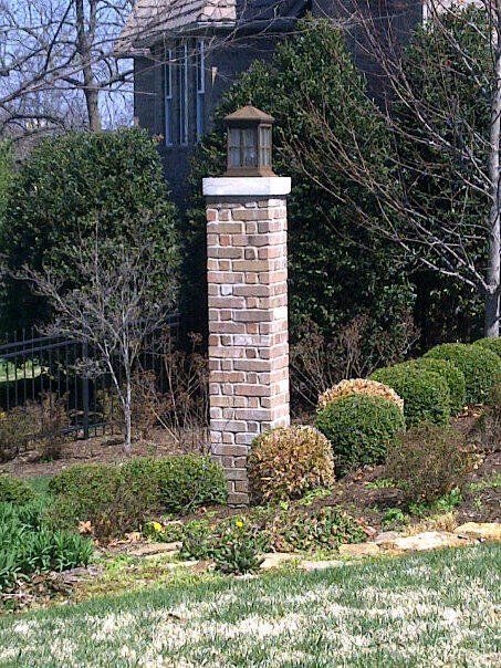 Brick garden pillar with a lantern cap amid shrubs and trees in a landscaped yard