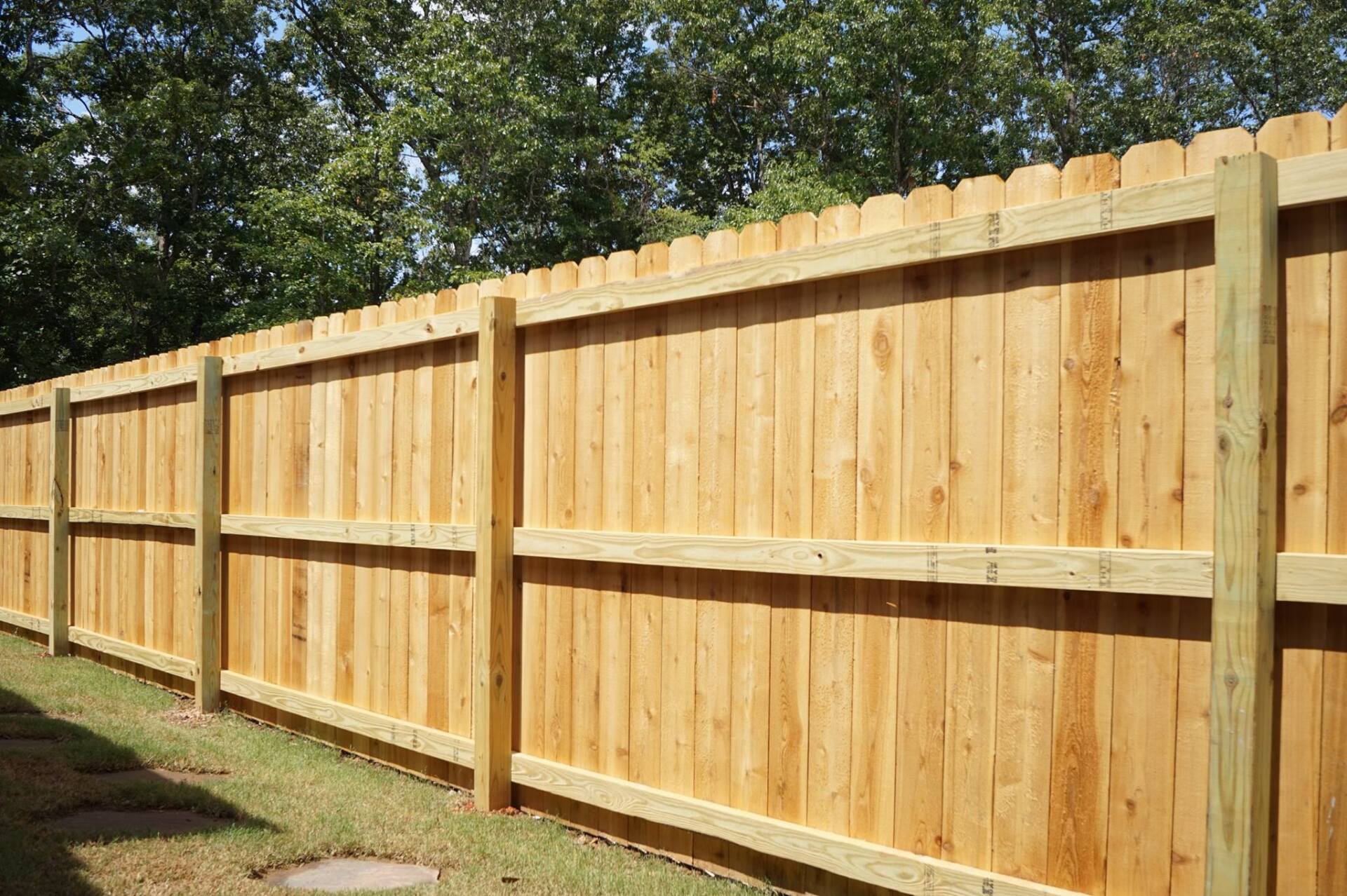Long wooden privacy fence in a grassy yard under trees