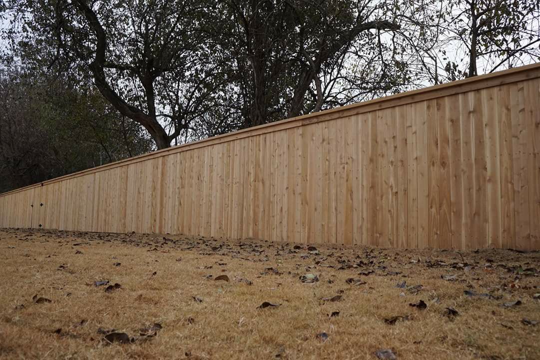 Long wooden fence along a dry, grassy slope with trees in the background