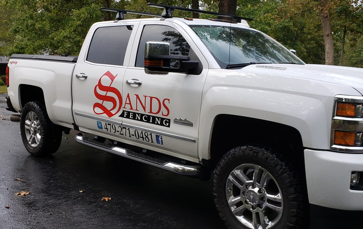 White pickup truck with Sands Roofing logo parked on a wet road near trees