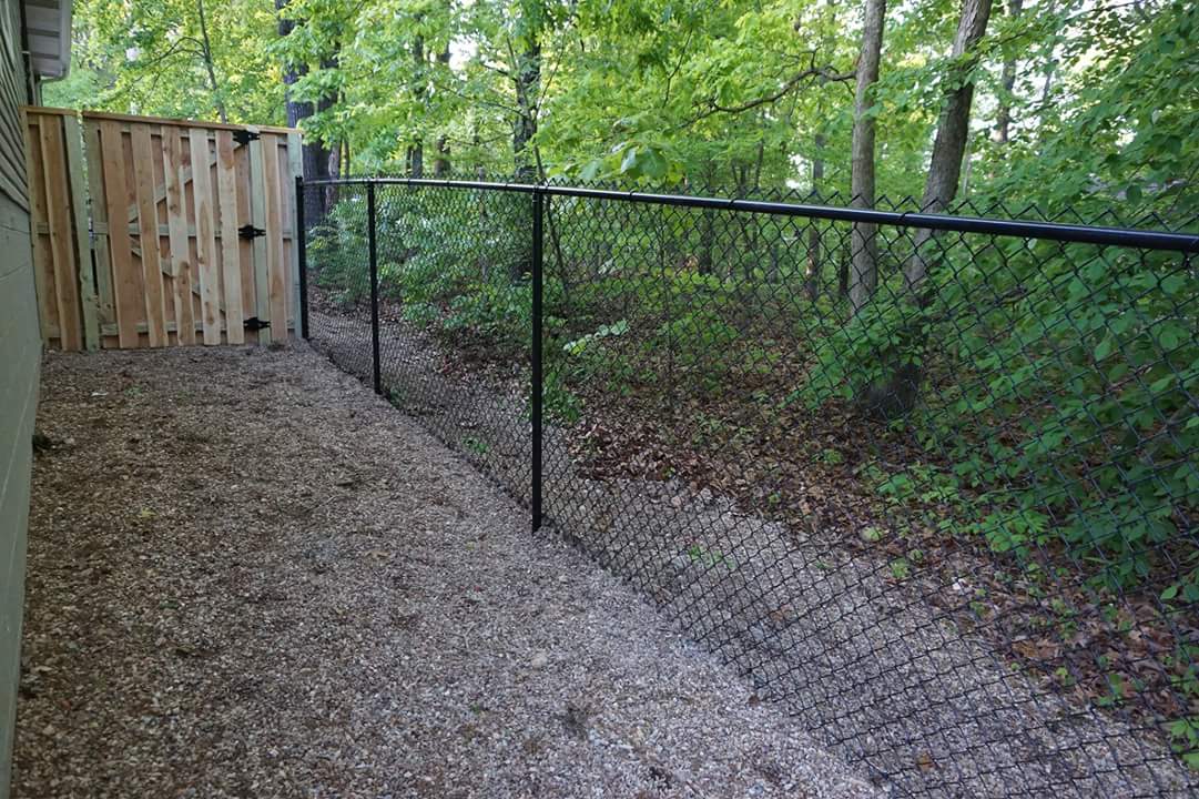 Gravel path beside a black chain-link fence and wooden gate in a wooded yard