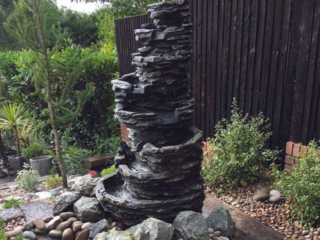 A water fountain in a garden with a black fence in the background.