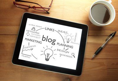 Tablet with blog-related keywords. A pen, coffee, and glasses rest on a wooden desk.