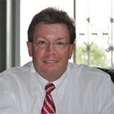 Man in white shirt and red striped tie, wearing glasses, smiling at the camera.