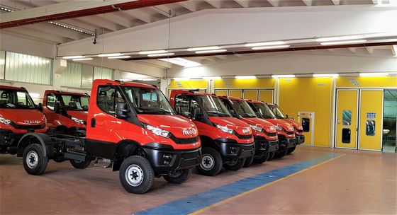 Una fila di camion rossi fuoristrada all'interno di un garage, accanto a pareti gialle e grandi porte.