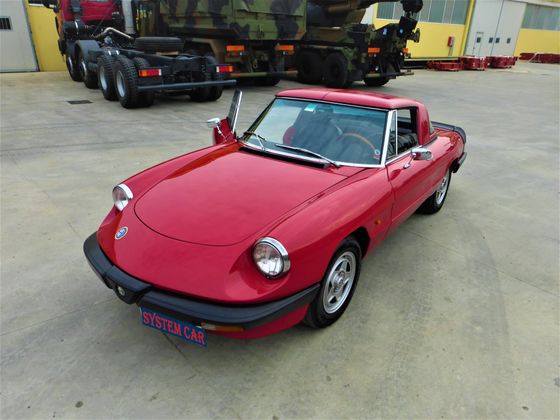 Alfa Romeo Spider rossa decappottabile parcheggiata all'aperto con la portiera aperta.