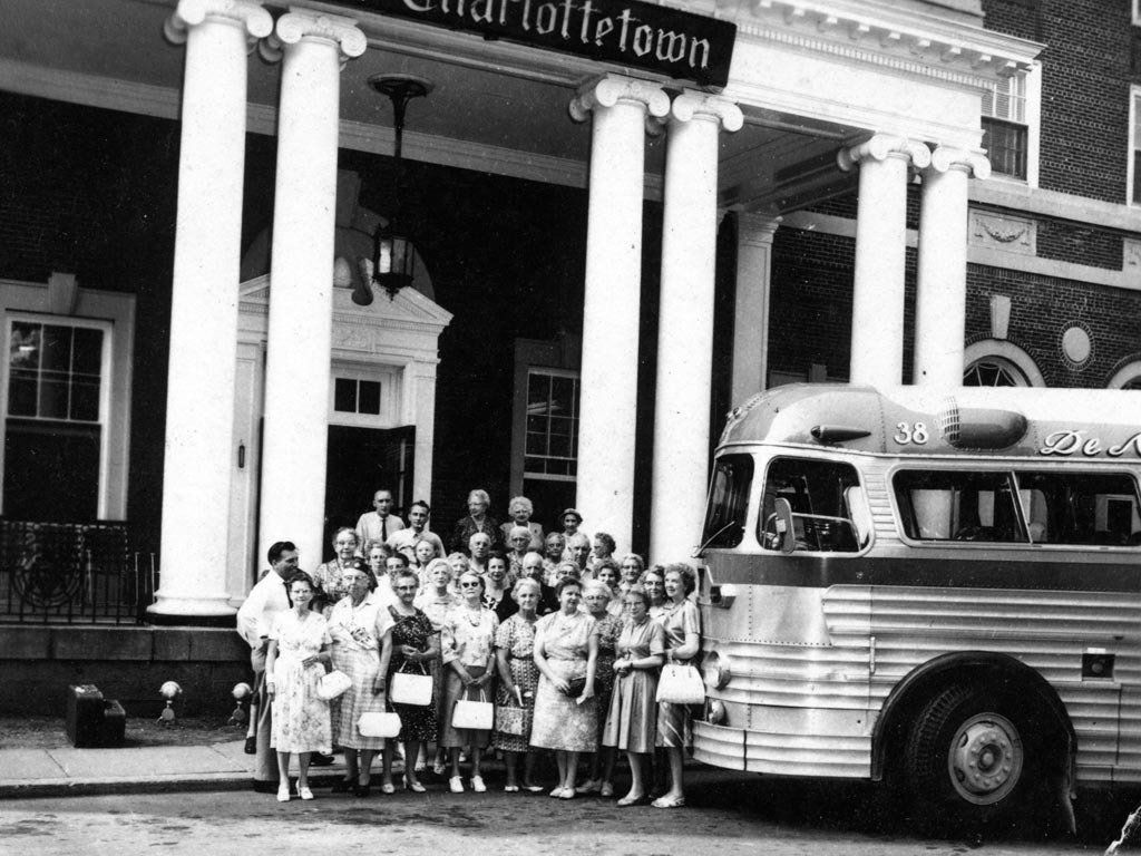 Group of women standing by a bus in front of a building with columns, 