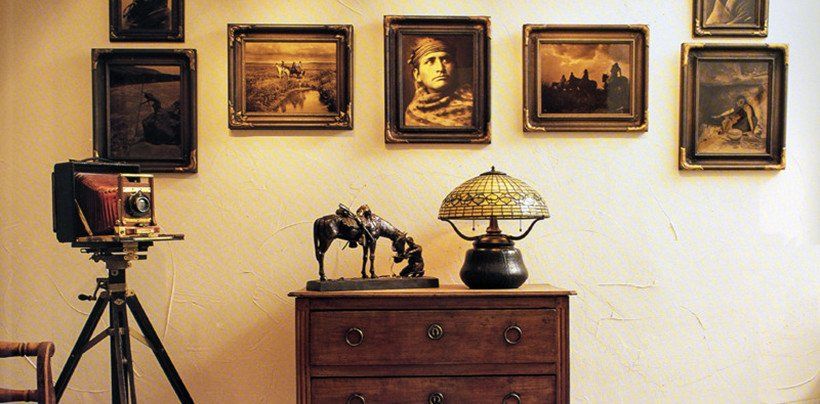 A room with a dresser a lamp and a camera on a tripod.