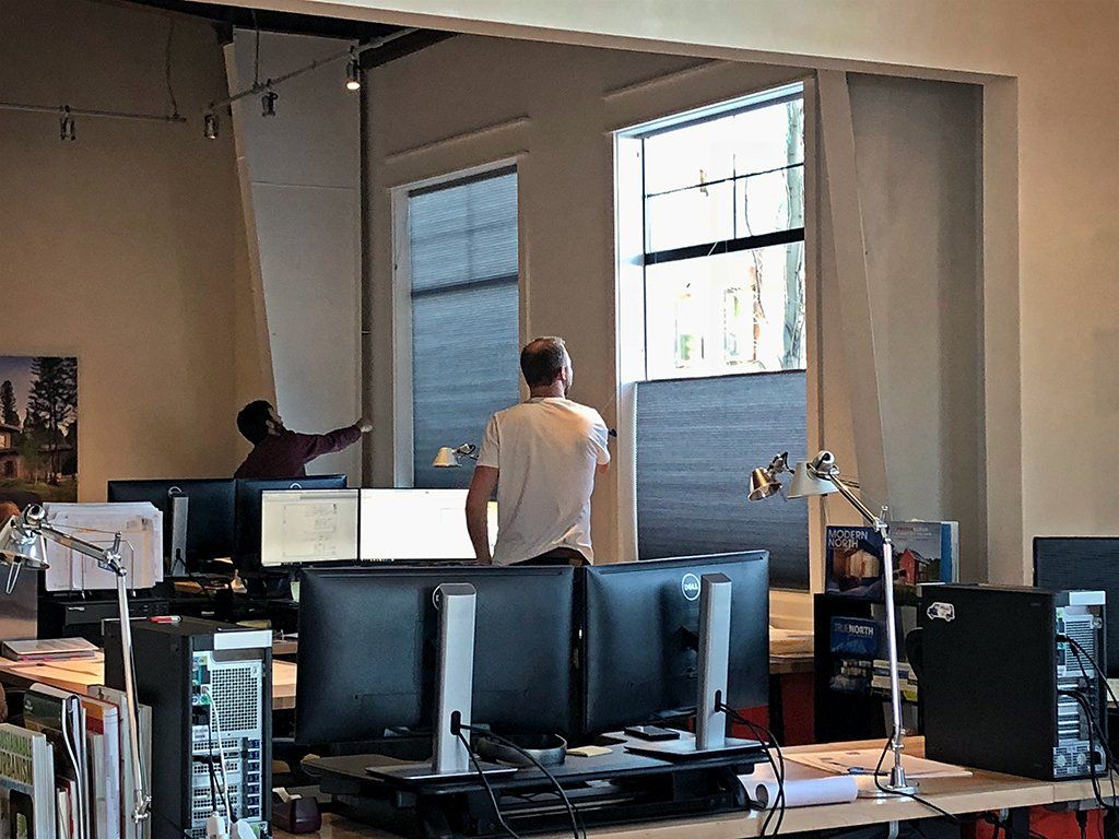 A man is standing in front of a window in an office surrounded by computer monitors.