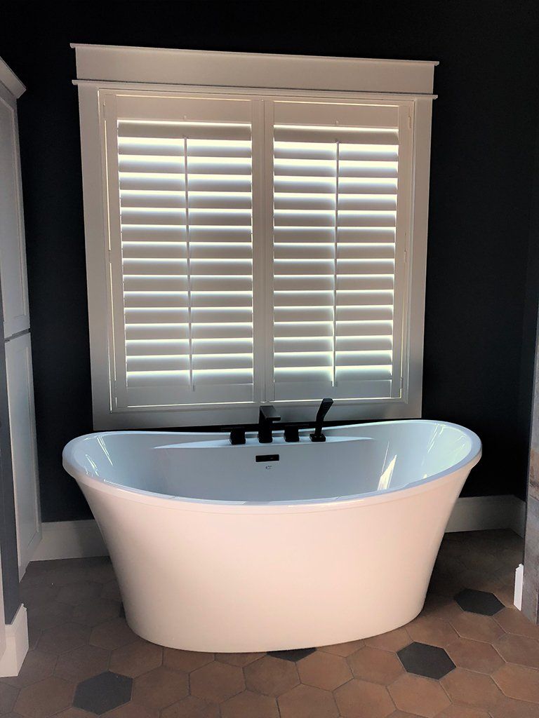 A bathtub in a bathroom with shutters on the window