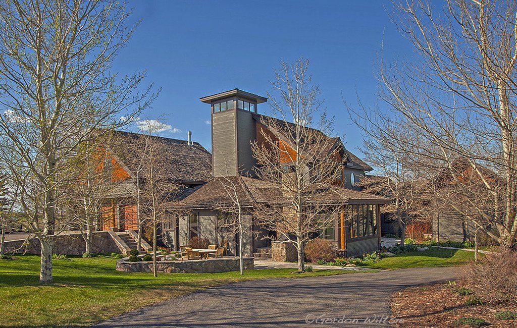A large house is surrounded by trees and grass on a sunny day.