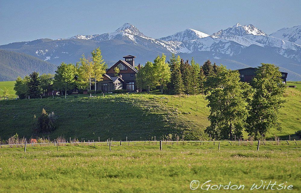 A house sits on top of a grassy hill with mountains in the background.
