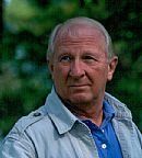 A man wearing a blue shirt and a grey jacket is looking at the camera.