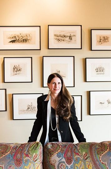 A woman is standing next to a couch in front of a wall of pictures.