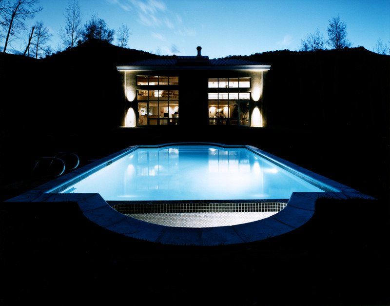 A large swimming pool is lit up at night in front of a house
