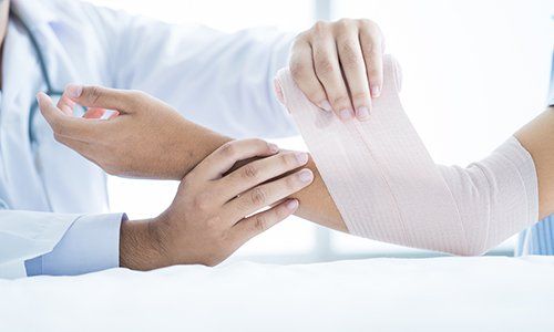 delle mani di un medico che applicano una fasciatura a un braccio di un ragazzo