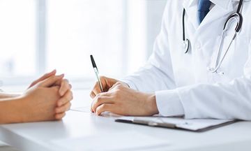 due mani di un medico appoggiate sulla scrivania con una penna